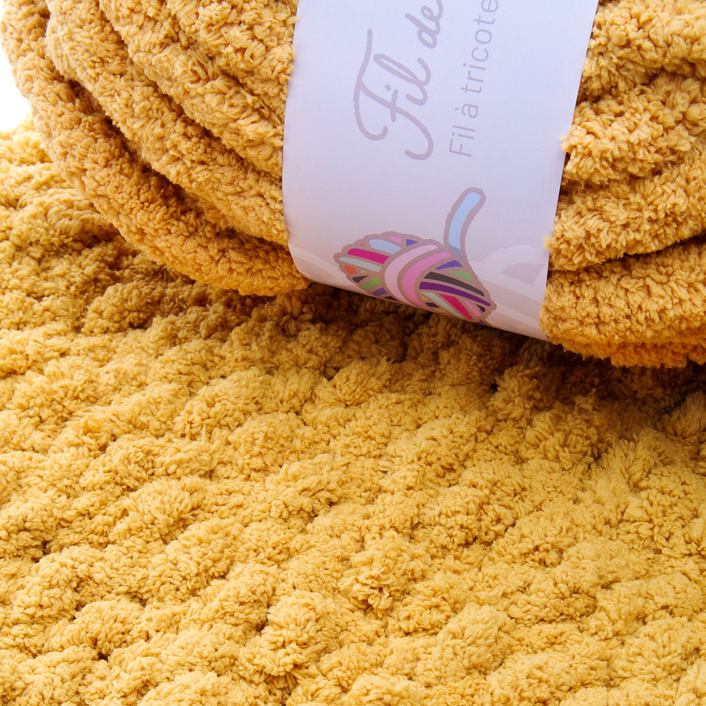 Couverture peluche chaude couleur miel avec étiquette papier « Fils de… Fil d’astricot » et motif spirale colorée. Or Moutarde.