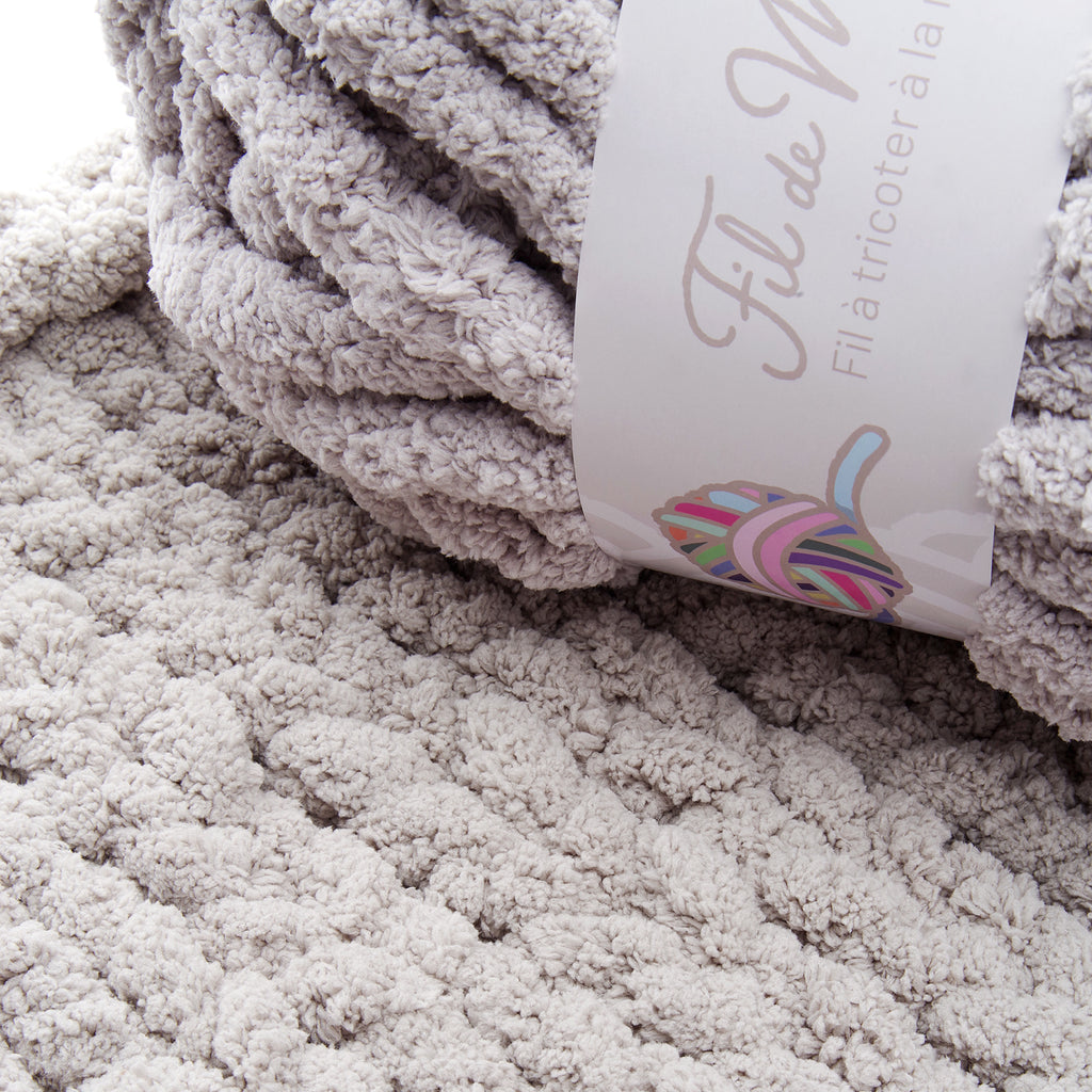 Texte en alt: Tête et texture d’une couverture en peluche couleur taupe avec étiquette blanche affichant le mot Taupe.