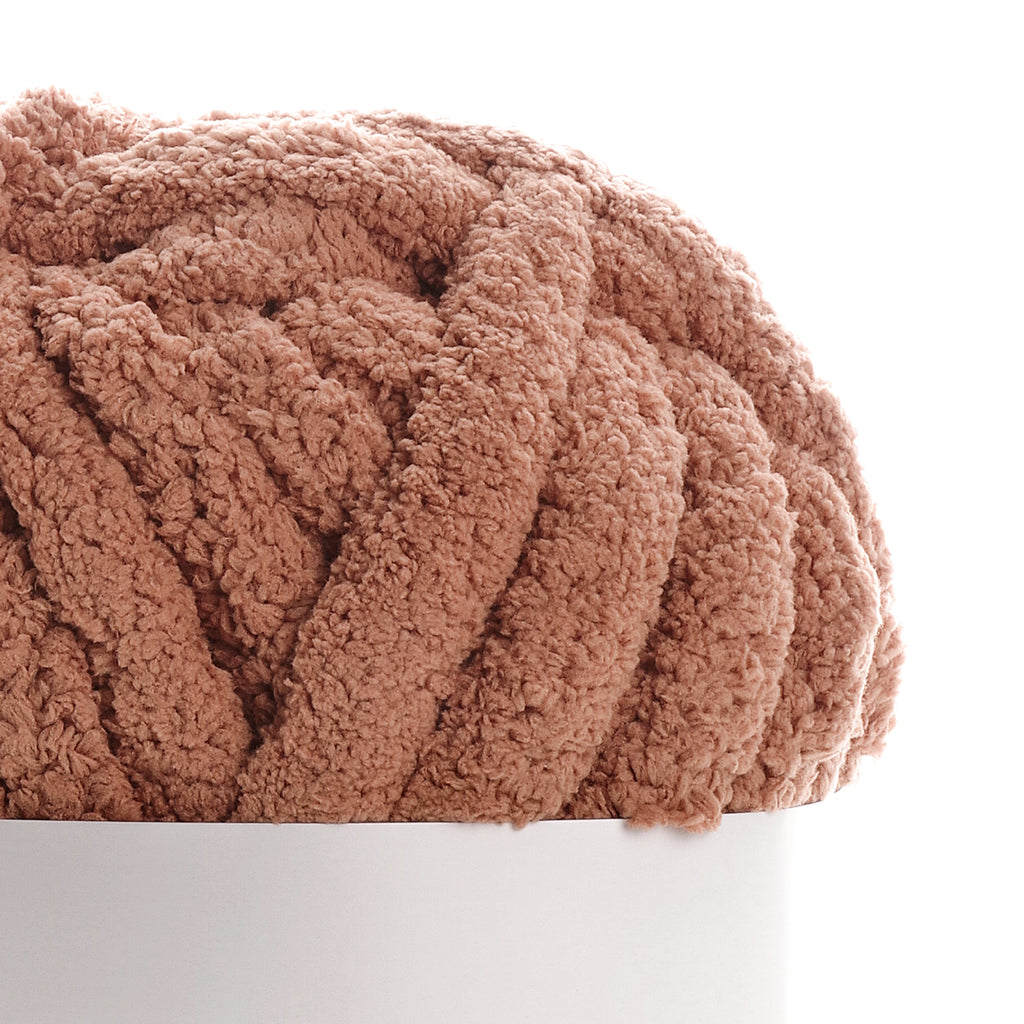 Texte alternatif : Écharpe ou couverture moelleuse couleur caramel en tricot bouclé reposant sur un socle blanc. Mot clé principal: Caramel.