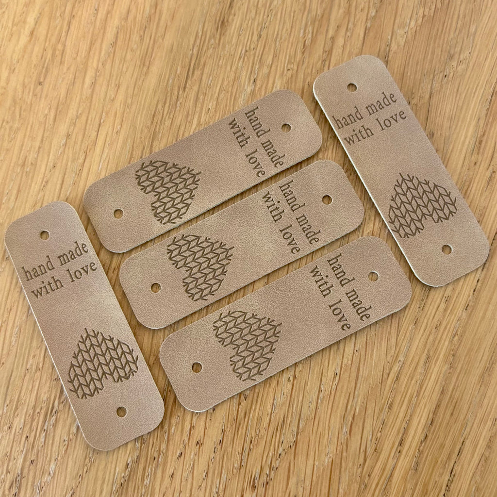 Étiquette de finition en simili cuir: tags beiges avec motif en forme de cœur et la mention “hand made with love” sur chaque étiquette perforée