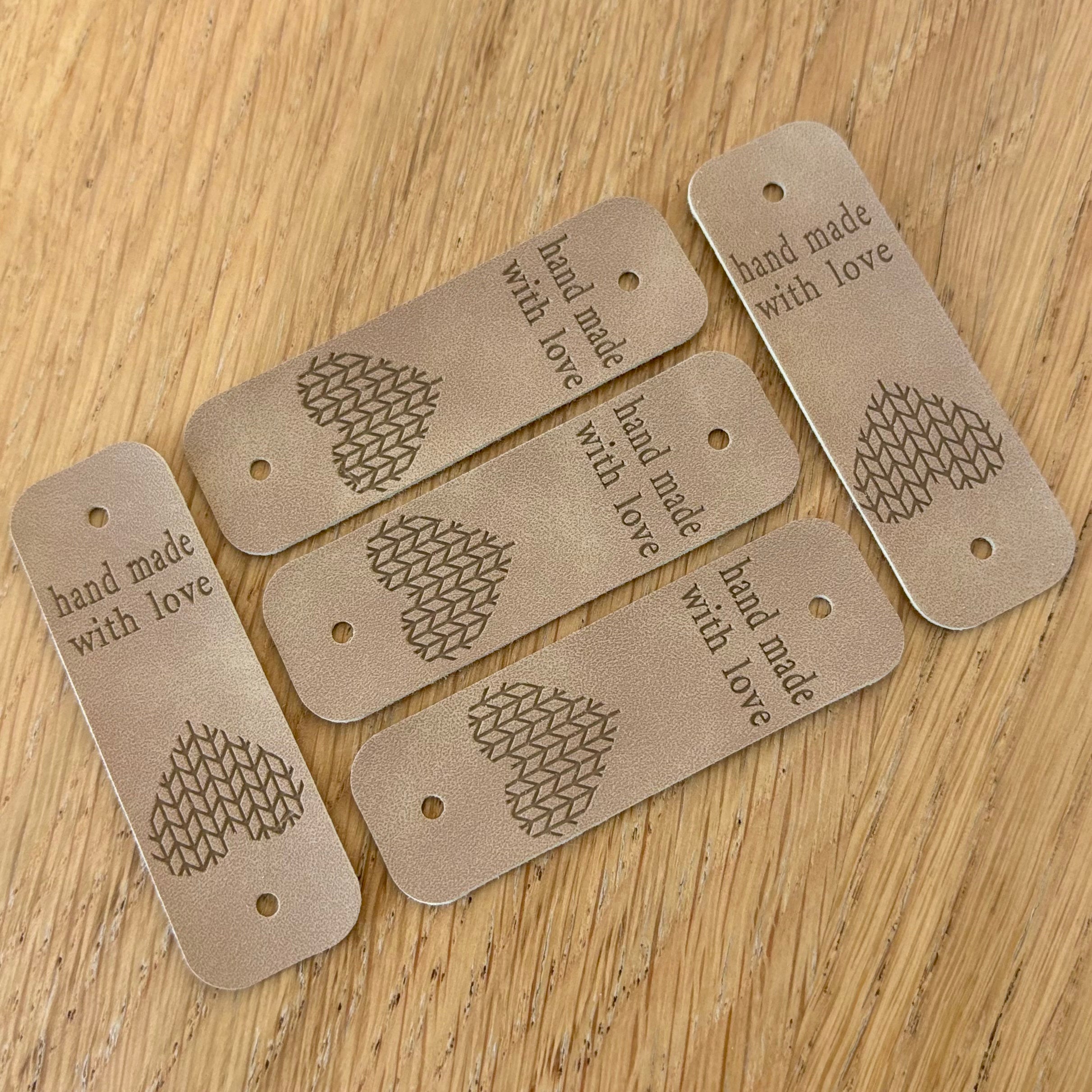 Étiquette de finition en simili cuir: tags beiges avec motif en forme de cœur et la mention “hand made with love” sur chaque étiquette perforée