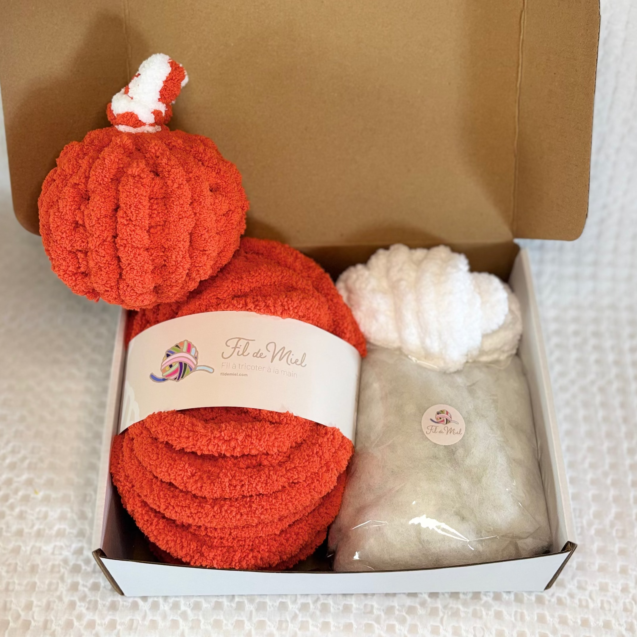Kit Citrouille Créatif – Spécial Halloween: pelotes de laine rouge et blanc dans une boîte, avec étiquette et sachet gris.
