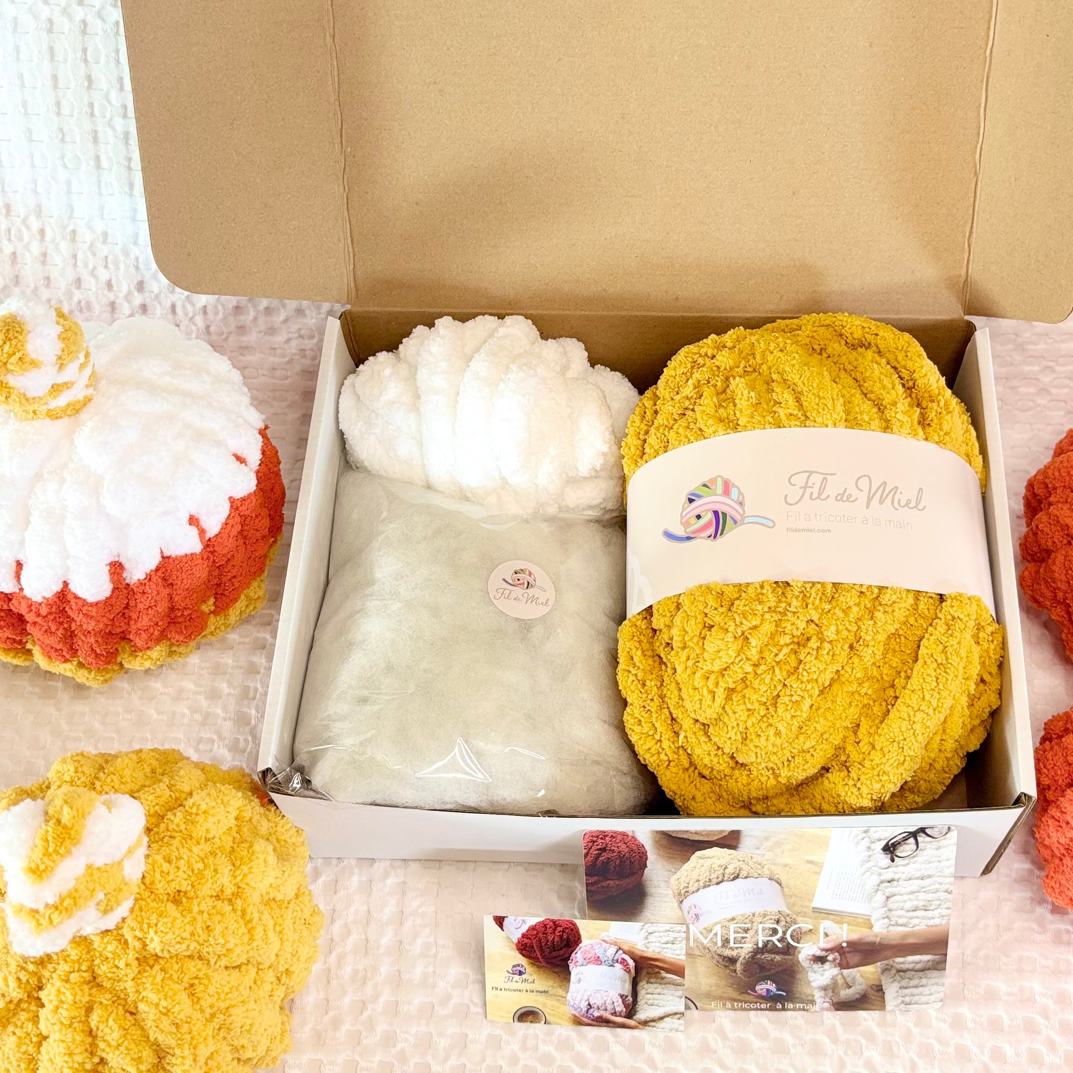 Kit Citrouille Créatif – Spécial Halloween: box contenant pelotes de laine côtelée orange, blanche et jaune, avec enveloppe et étiquette “Fil de Miel”, sur fond beige.