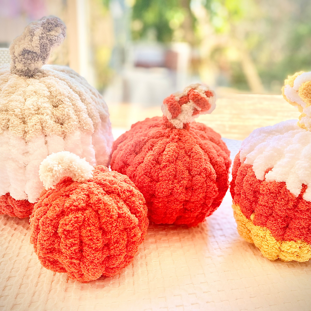 Pommes de crochet colorées en forme de citrouilles, rouges et blanches, sur une surface lumineuse.